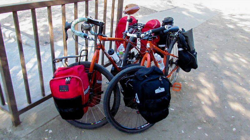 Front view of 2 bikes, side by side, parked on pavement, in front of a railing