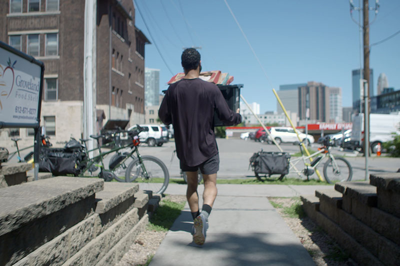 Person walking toward parked cargo bikes carrying bin of food