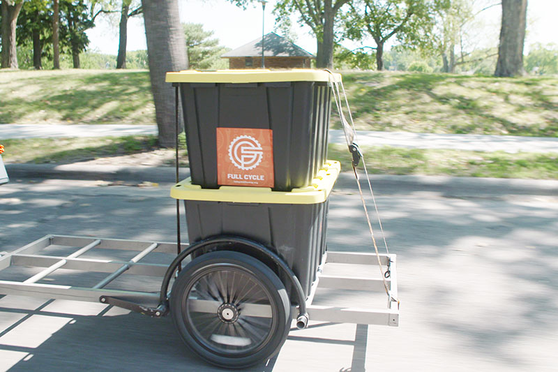 Two large bins stacked and ratchet strapped to Surly trailer during delivery on neighborhood street