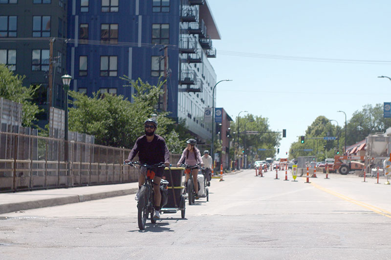 Group of cyclists riding cargo bikes pulling trailers in city street to delivery food