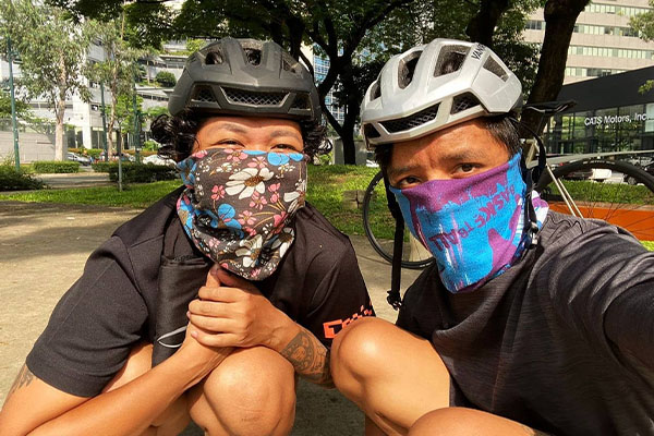 Aneka with brother, kneeling posting for photo with bike helmets and face coverings outside, bikes behind