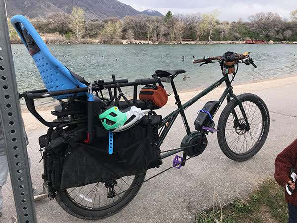 Surly Big Easy parked at beach, with kid seat connected to back, helmet hanging from bike, mountains in background