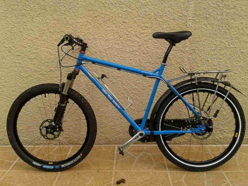 Left profile of a blue Surly Troll bike on a block sidewalk, in front of a tan stucco wall