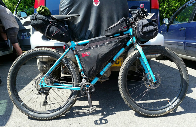 Right side profile  of a Surly bike, turquoise, with a front and seat pack behind a van