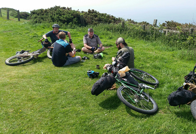 Four cyclist sitting on the grass with their bikes, loaded with gear, laying next to them