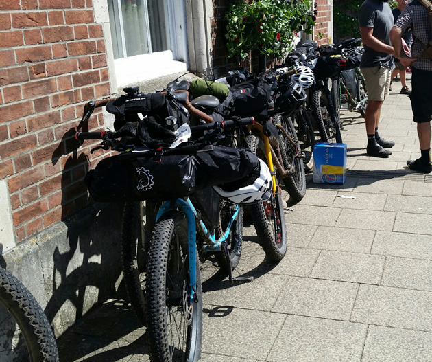 Bikes on a cement block sidewalk are lined up against a red brick building 