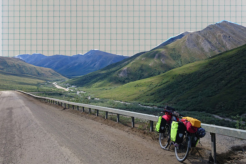 Fully loaded touring bike leaning against guard rail on valley road river and mountains in background 