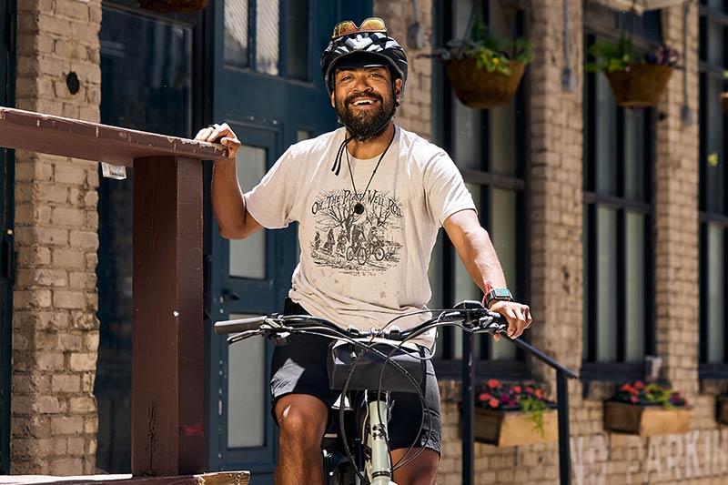 Alexis smiling while sitting stopped on Surly Skid Loader bike holding onto railing in front of building