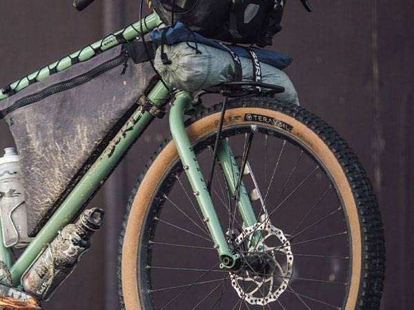 Side angle front view of Surly Grappler bike loaded for bikepacking with water bottles, frame pack and front rack