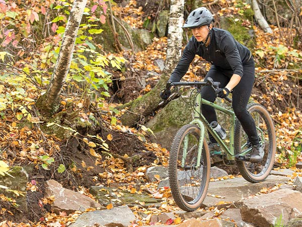 Person out of the saddle descending rocky forest trail section on Surly Grappler, hands in the drops