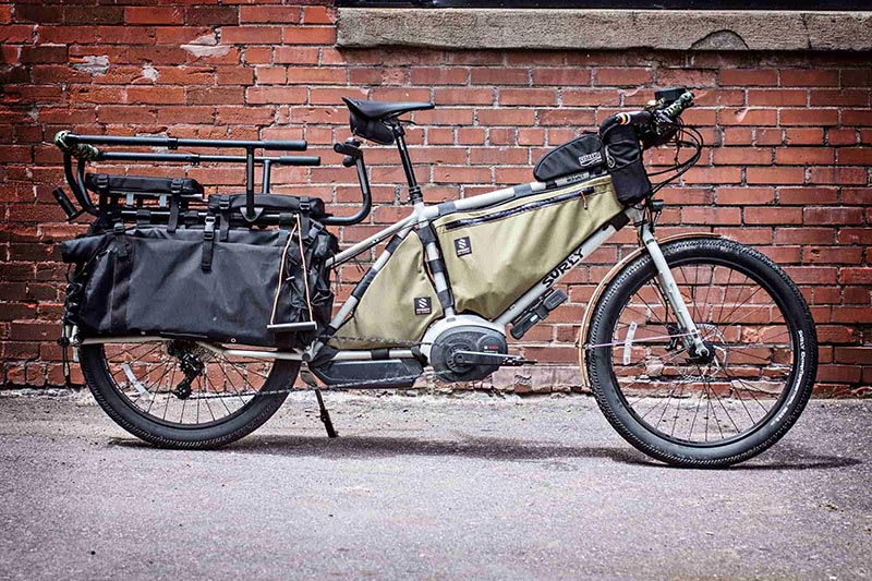 Right side view of a white Surly Big Easy bike with gear packs and rear rack in front of a red brick building