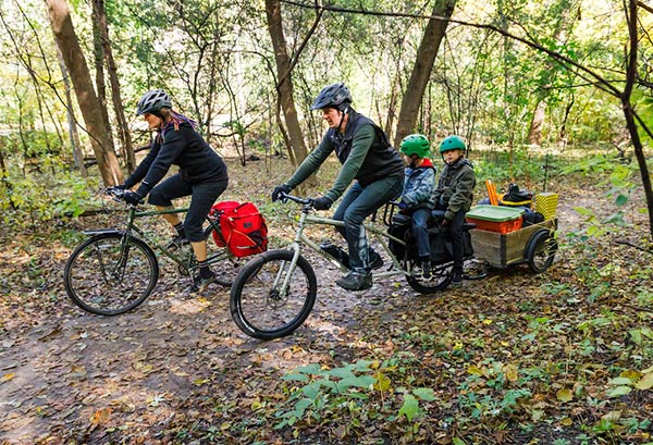 Two cyclist riding on a woodsy trailer with one rider on a Surly Bike Easy bike with two children and a trailer