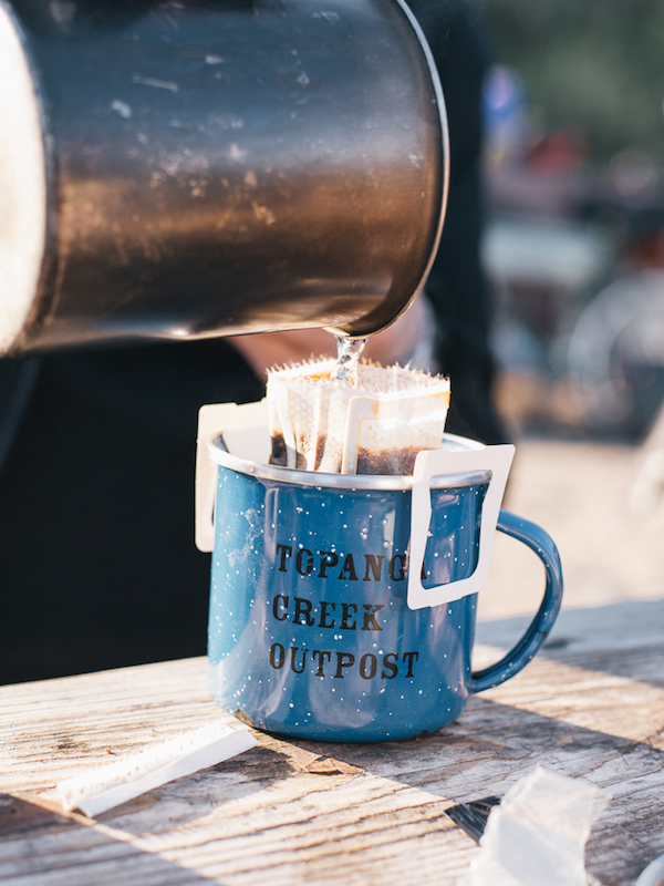 A large steel cup pours water into a smaller blue steel cup sitting on a wood table