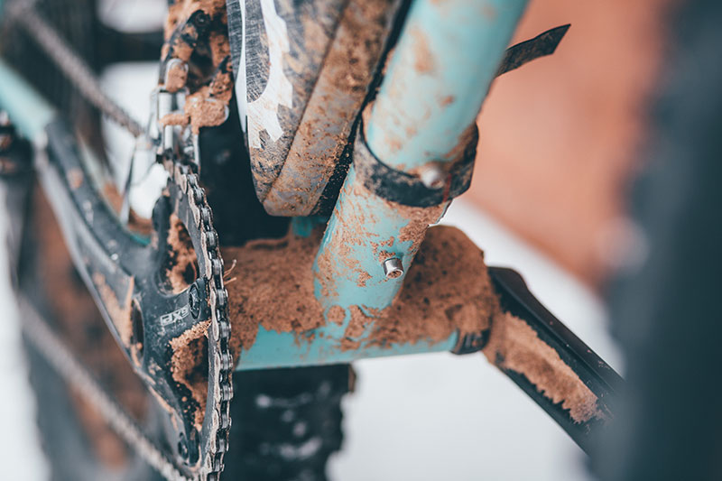 Close-up of crank and underside of downtube and bottom bracket of bike covered in gravel mud