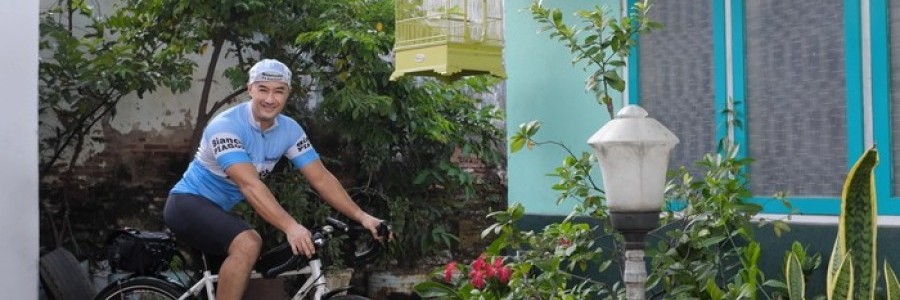 Cyclist sitting a white Surly Midnight Special bike with a seat pack poses in front of a home with plants and shrubbery