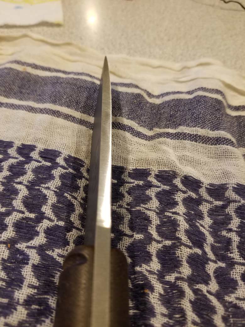 Downward view of a knife with black handles laying horizontally of it's spline with blade facing up on a woven towel