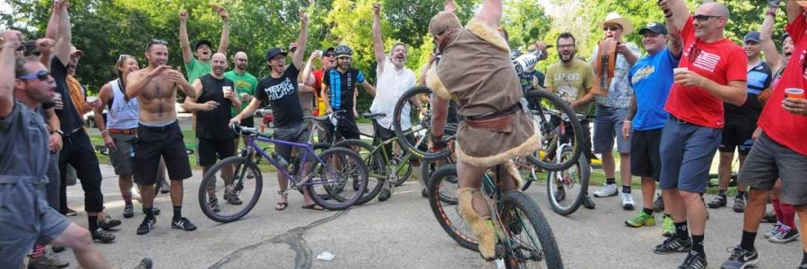 Cyclists ride up an icy road on fat bikes  in the woods with front cyclist wearing viking clothing