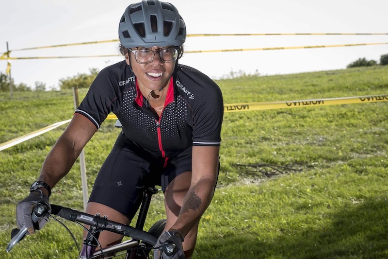 Front view of a cyclist on a bike, turning a corner on trail in the grass with caution tape around it