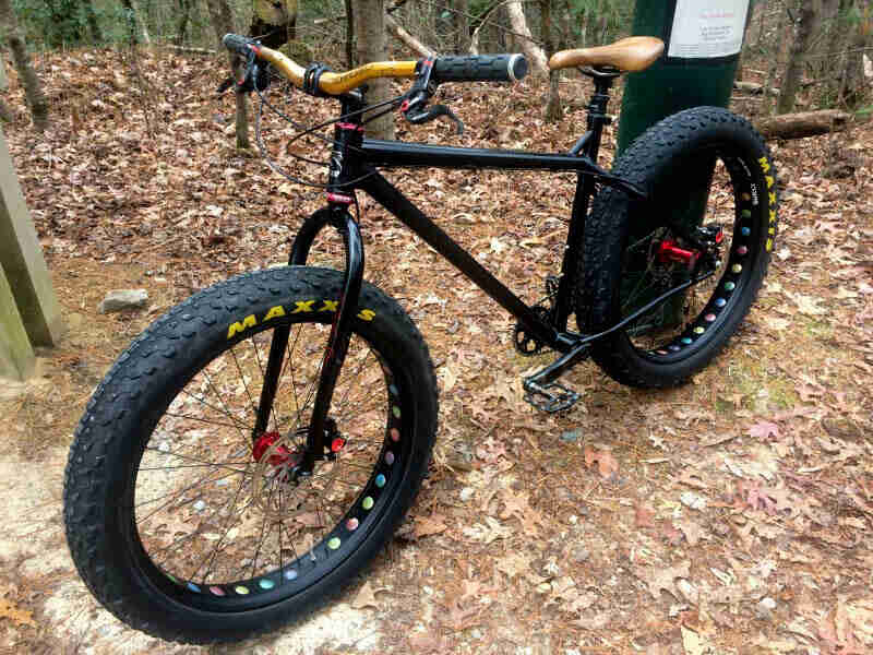 Front left view of a black Surly fat bike, standing on top of grass and leaves, with trees in the background