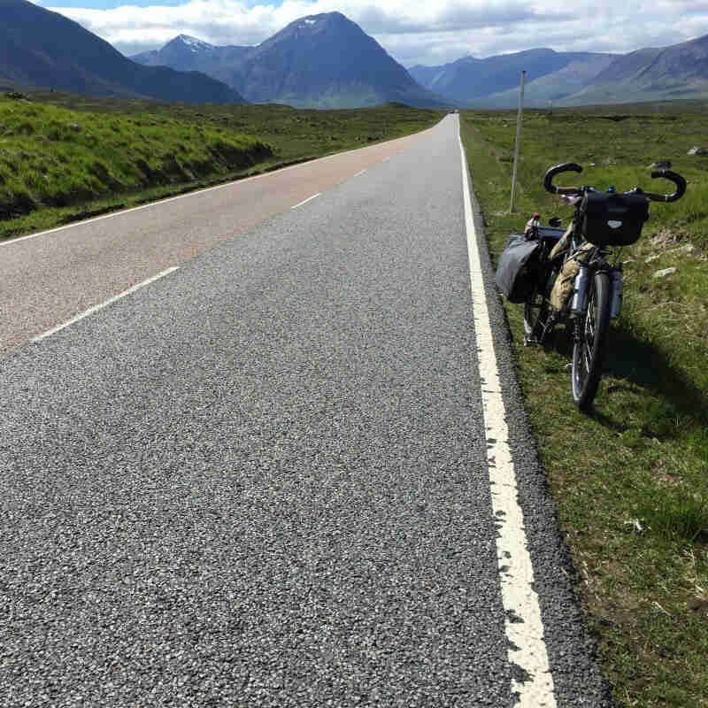 Front view of a Surly Big Dummy bike, parked on the side of a highway, with green fields and mountains in the background