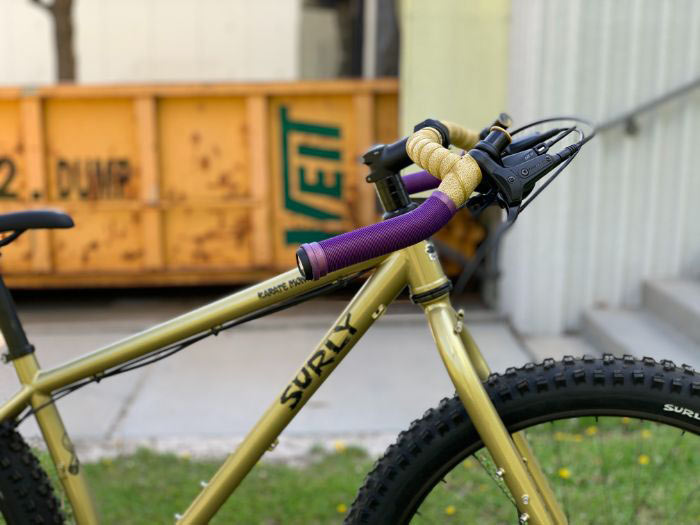 Side view of Corner Bar on bike with purple mountain grips on drops and gold bar tape on top, yellow dumpster in background