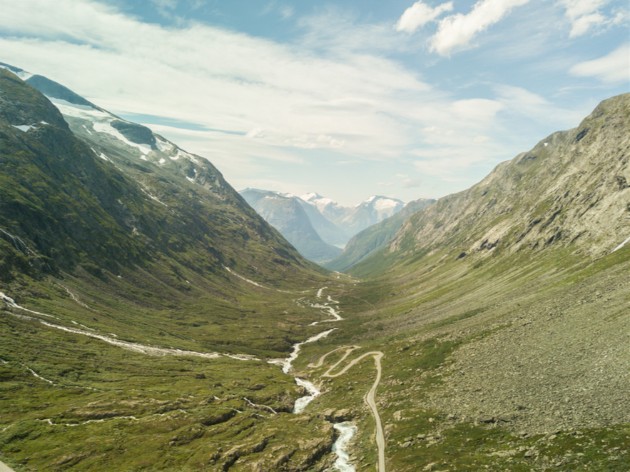 Green mountain range with a narrow stream flowing in between with clouds and blue sky above