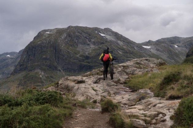 A cyclist walking with their bike up a rock hill in the mountains