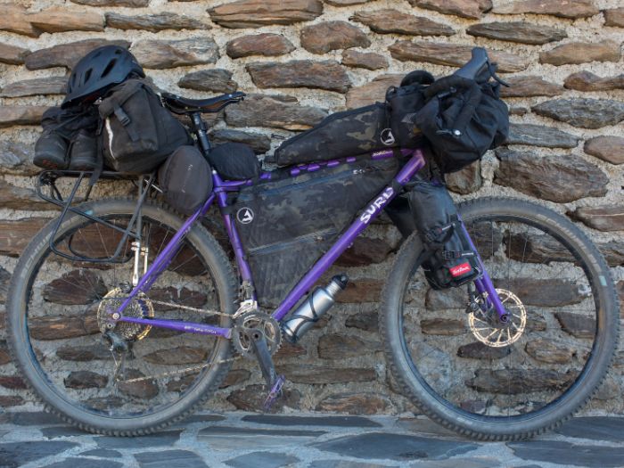 Ride side view of a custom Surly Karate Monkey bike loaded with gear leaning  on a stone wall