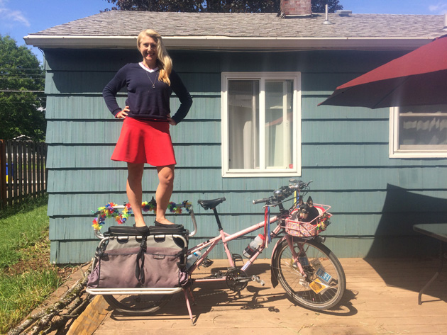 Madi Carlson standing with hands on hips, on the back rack of a Surly Big Dummy bike, custom painted in pink