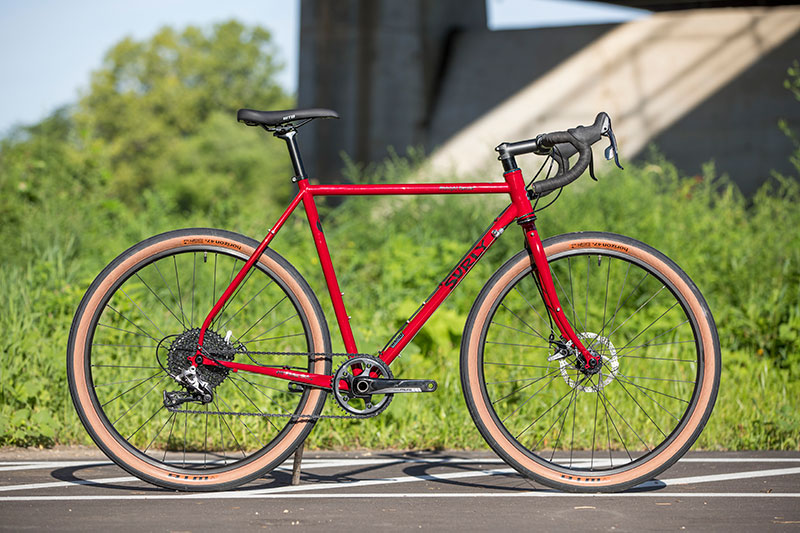 Red Surly Midnight Special complete bike side view, held up by stick in parking lot on sunny afternoon in summer