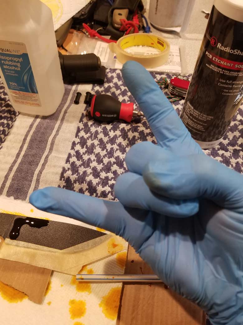 Downward view of hands in nitrile gloves with horns sign, over a bottle of isopropyl alcohol and PCB etchant solution