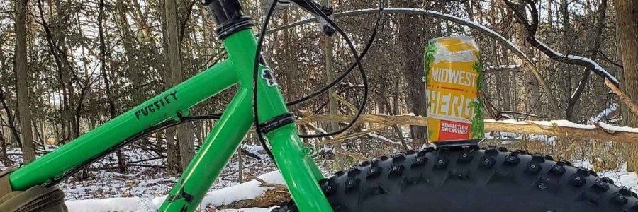 Right side, cropped view of green Surly Pugsley fat bike, with a beer can on the front tire, in the snowy woods