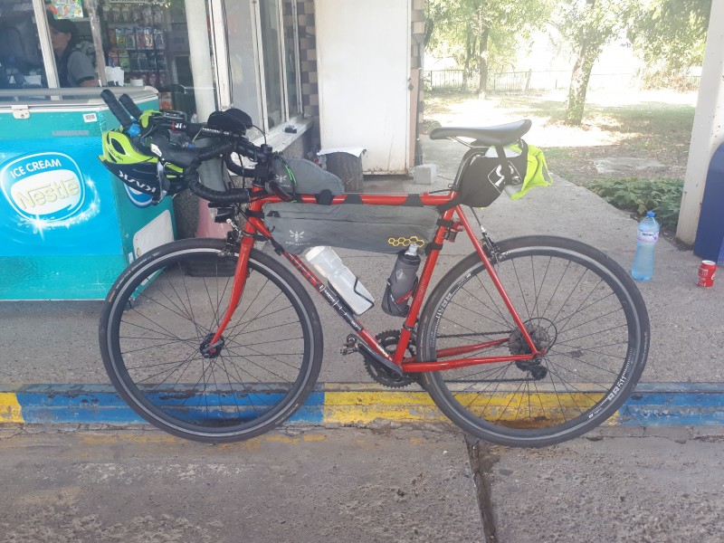 Left side view of a Surly Pacer bike, red, standing against a street curb at a store front