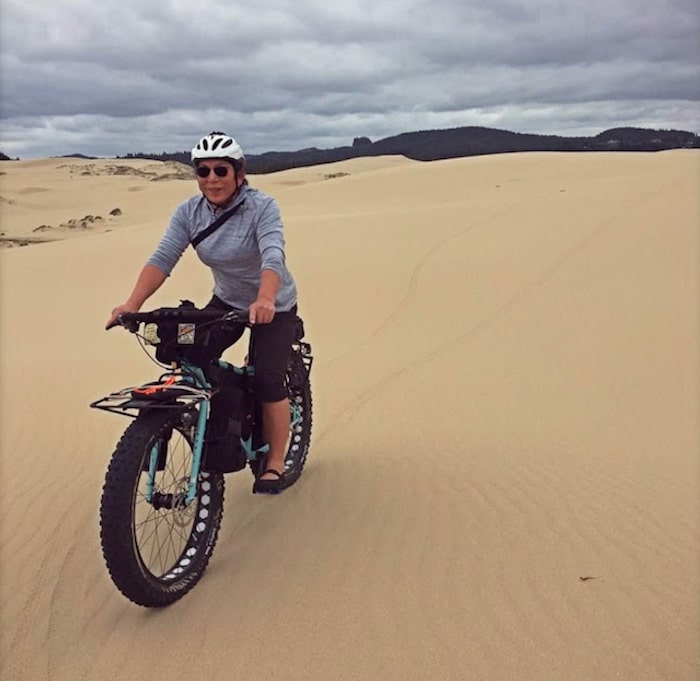 Cyclist on mint color Surly Ice Cream Truck bike riding through a sandy desert with hills in the distance