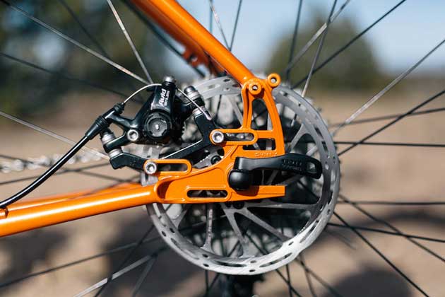 Zoomed in left side view of the rear axle plate, brake disc and brake caliper of a Surly Pugsley fat bike, orange