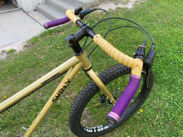 Surly Karate Monkey with Corner Bar installed with purple mountain grips installed in the drops and gold bar tape on the top