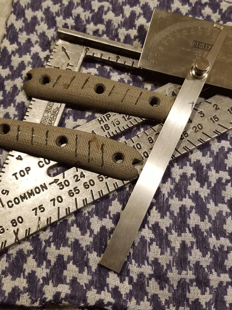 Two tan knife handle halves with three holes with an angle gauge on top of a carpenter's square laying on woven towel