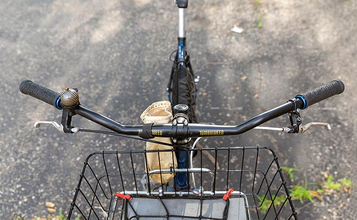 Front view looking down at front rack/basket with webbing to secure items, handlebar with grips, brake levers and bell