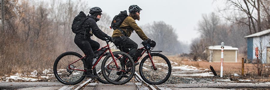 Two bike commuters riding on road in warm clothing, helmets and backpacks in light snow