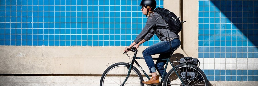 Cyclist rides a Surly bike on a sidewalk alongside a building with blue tiles on it