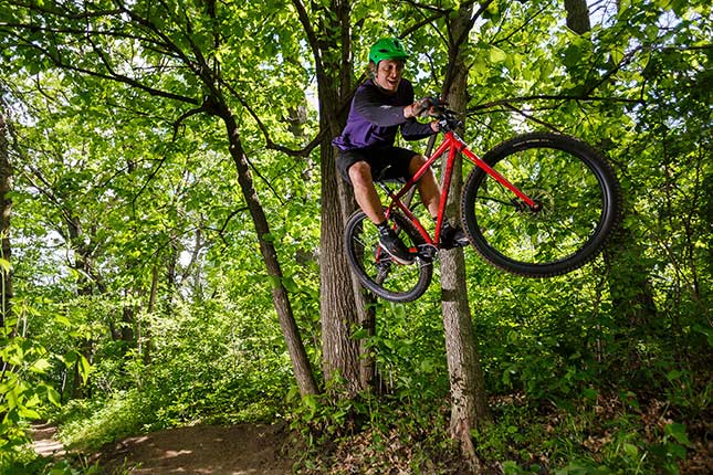 Mountain biker with green helmet jumping red Surly Krampus on off-road trail in the woods