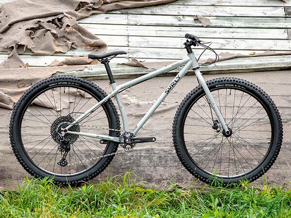 Surly Krampus bike side view with rigid fork, parked next to old building with tall grass