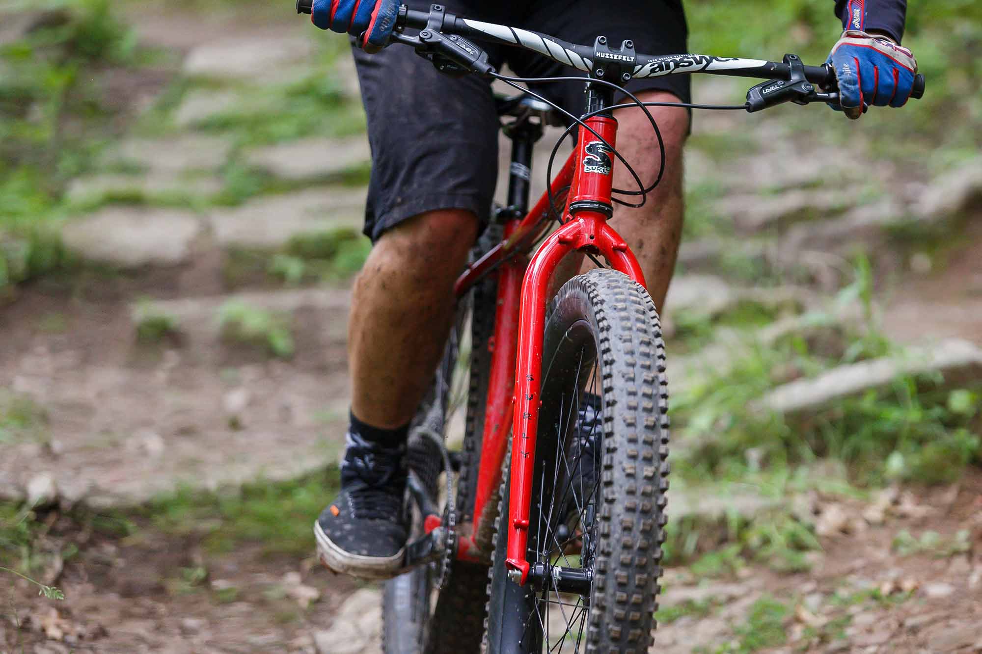 Mountain biker on rocky off-road trail riding red Surly Krampus showing large Surly Dirt Wizard tires on wide rims