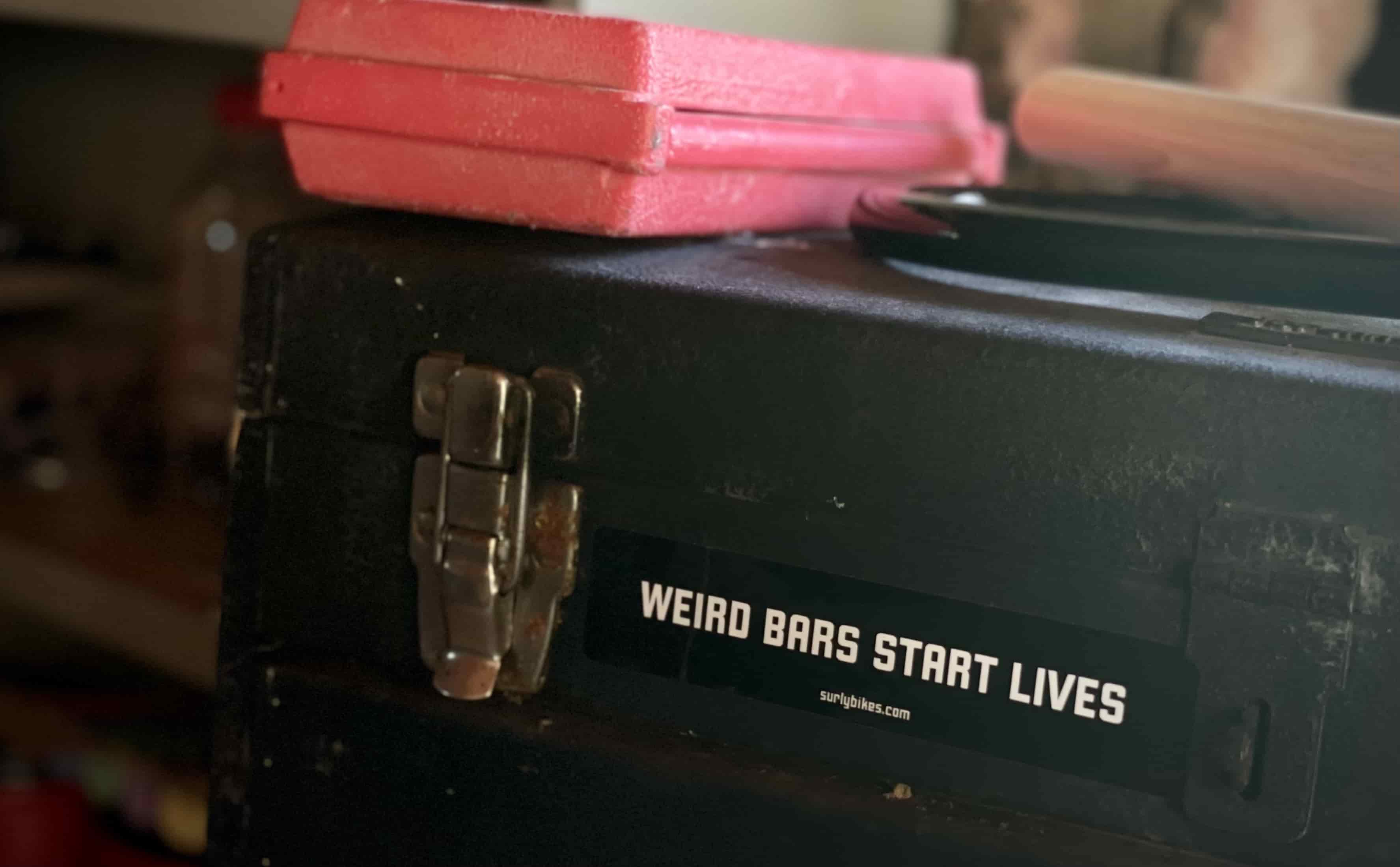 Black sticker on toolbox that says, “weird bars start lives”