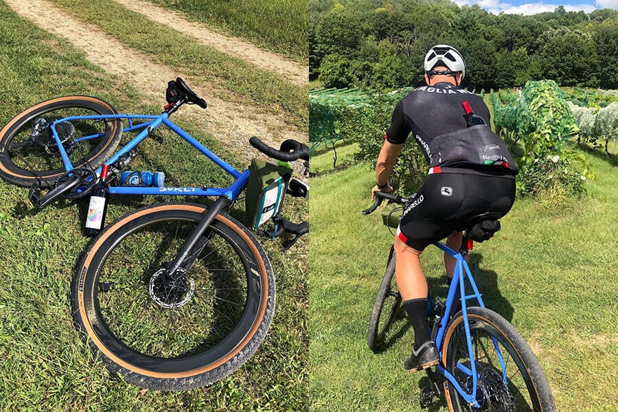 Surly Midnight Special bike lying in grass with bottle of wine and cyclist rides down grass hill of vineyard