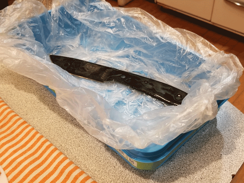 Black knife blade soaking in clear, plastic lined paint tray that's sitting on top of a white mat